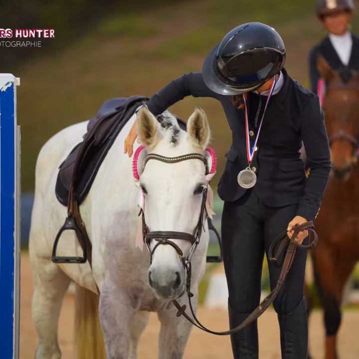Cavalière médaillée flattant son poney gris après l’épreuve