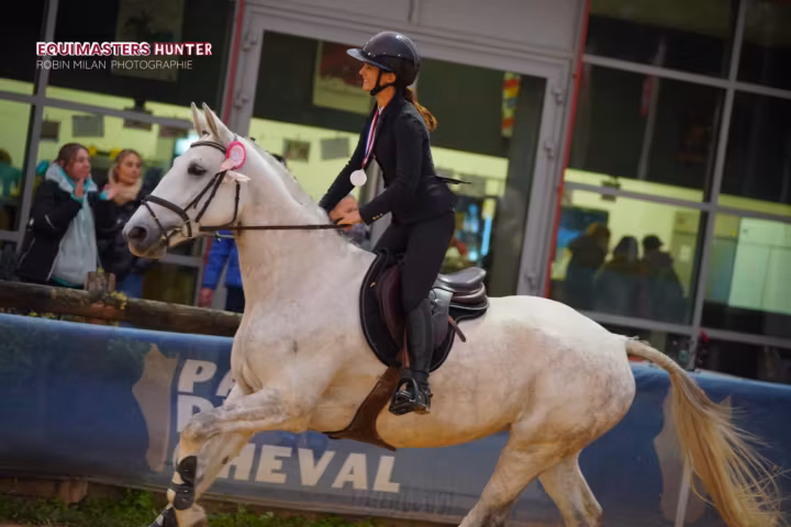 Cavalière au galop sur un poney gris devant les tribunes d’un concours de hunter