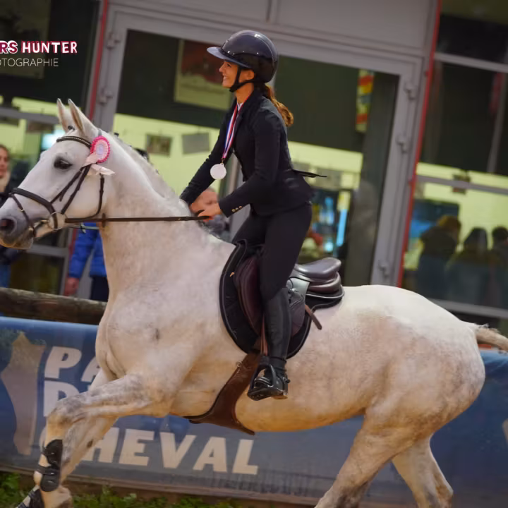 Cavalière au galop sur un poney gris devant les tribunes d’un concours de hunter
