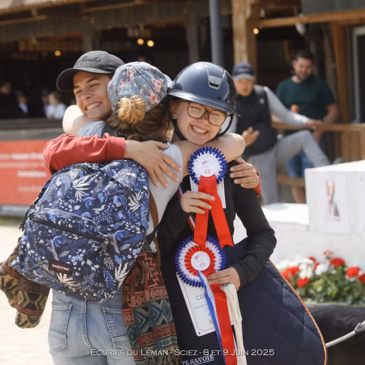 Cavalière casquée, cocardes à la main, serrée dans les bras de ses proches après la remise des prix