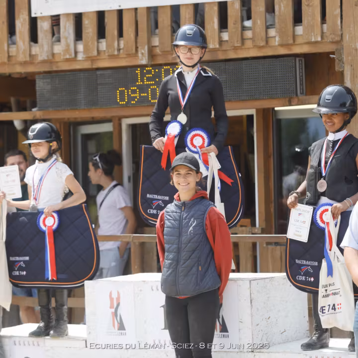 Jeunes cavalières médaillées sur le podium d’un concours, avec cocardes et tapis de selle